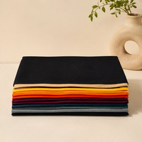 Stack of colorful folded cloths on a beige surface with a plant in the background