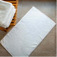 White towel on a tiled floor with a wooden basket containing more towels.