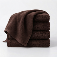 A stack of dark brown cotton towels with one larger towel draped over the top, photographed on a clean white studio background.