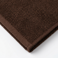A close-up of a folded brown terry cloth towel showing its textured surface and reinforced corner on a white background.